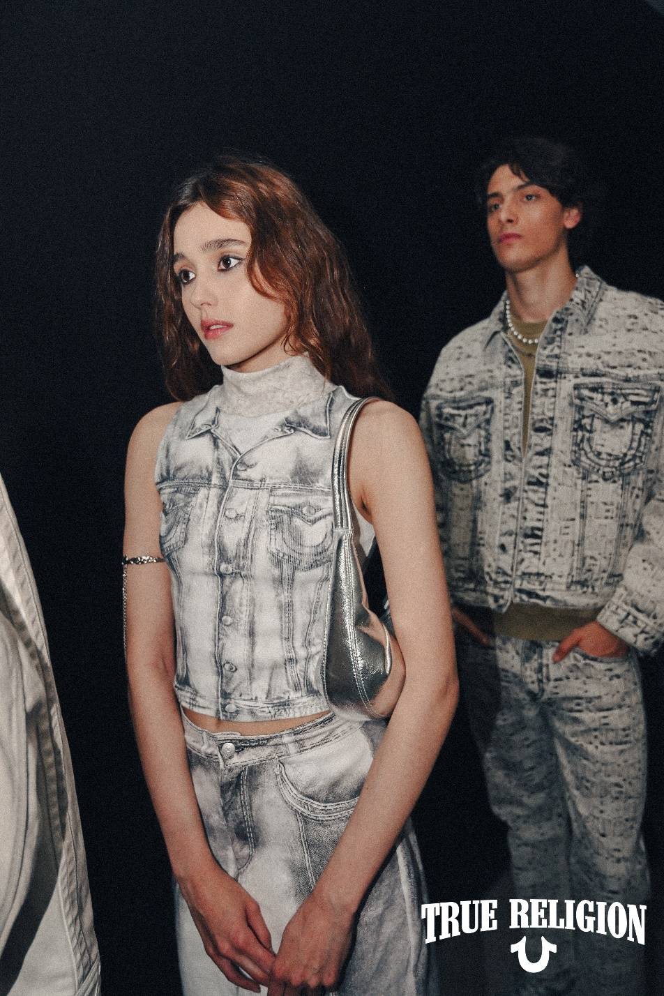 A person in a white vest and jeans

Description automatically generated